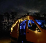 Experience cozy nights with our rv rental! A campervan adorned with warm string lights, blue interior, parked under a dark sky.