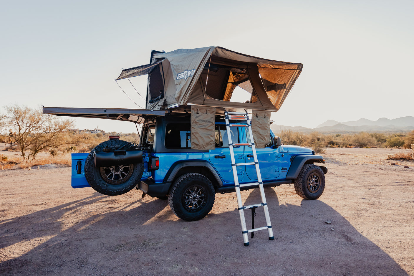 Blue Jeep with rooftop tent set up in desert for camping. Consider this rugged RV rental for your next adventure!