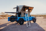 Blue Jeep with rooftop tent set up in desert for camping. Consider this rugged RV rental for your next adventure!