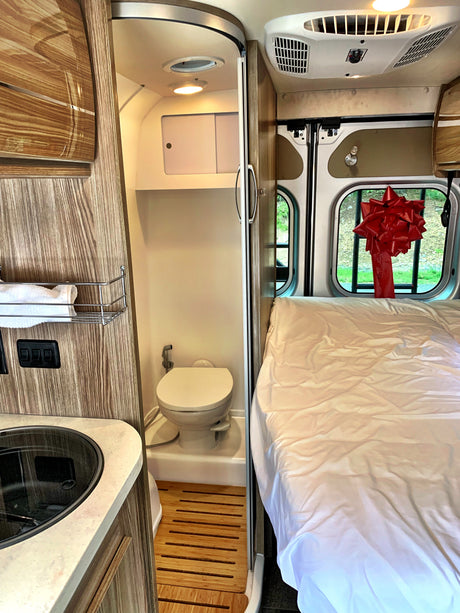 Inside this RV rental: a cozy bed, compact kitchen with sink, and a wet bath with toilet. Notice the red bow!