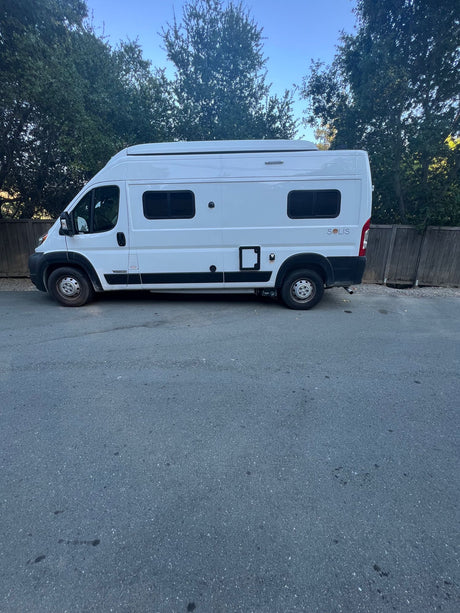 White Winnebago Solis camper van. Ideal RV rental for travel adventures & van life. Parked on asphalt near trees.