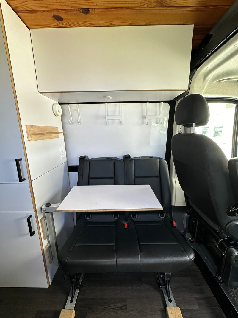 Modern RV rental interior with dual black leather seats, a flexible white table, and integrated white storage cabinets. — photo 11