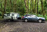 Explore nature with an rv rental! Subaru Outback towing a Cricket camper amidst towering, moss-covered trees.