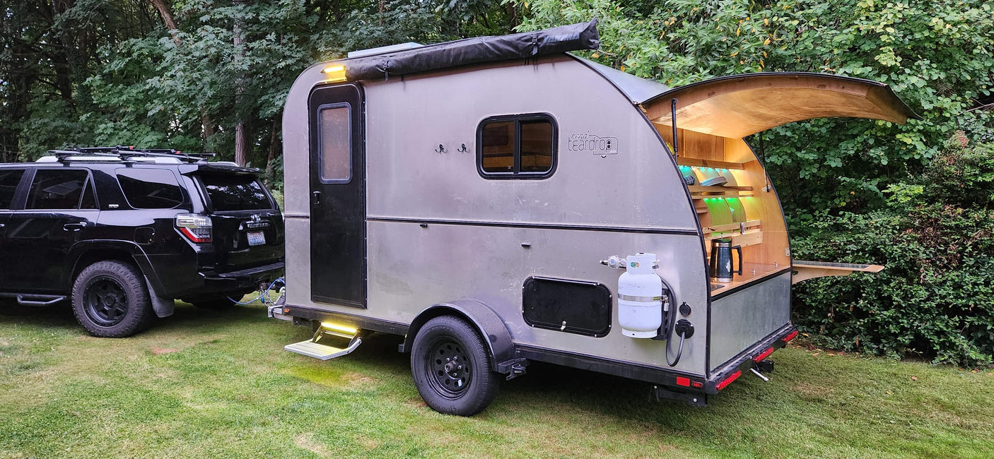 A stylish teardrop trailer with an illuminated outdoor kitchen, ideal for an RV rental and cozy camping adventures.