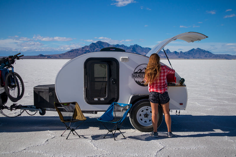 Enjoying the open road! Woman setting up her RV rental teardrop camper kitchen on vast salt flats with mountains in view. Adventure camping. — photo 19