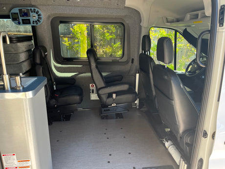 Spacious RV rental interior featuring versatile passenger seating, a compact sink, and control panel, ideal for road trips.