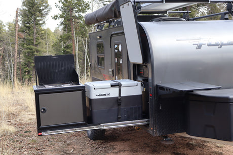 RV rental's outdoor kitchen featuring a Dometic fridge and stove, pulled out from the camper in a forest.