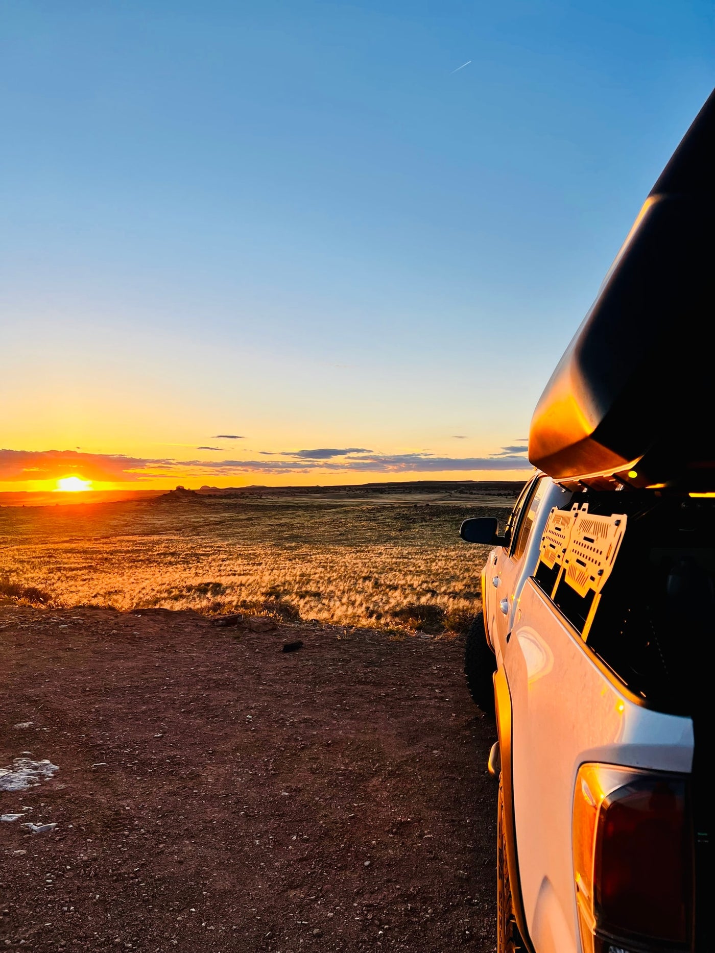 White pickup truck with rooftop camper faces a golden sunset over fields. Ideal RV rental scene for nature exploration. — photo 5