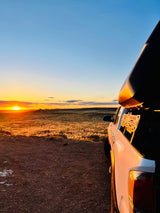 White pickup truck with rooftop camper faces a golden sunset over fields. Ideal RV rental scene for nature exploration.