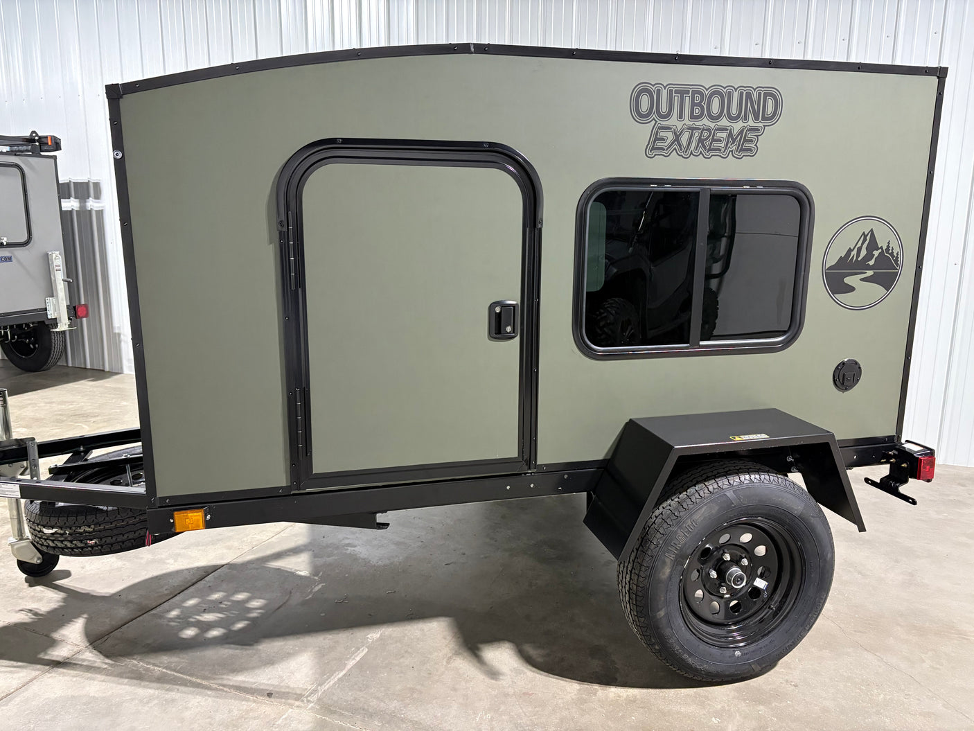 Olive green "Outbound Extreme" adventure trailer, featuring a side door and window. Perfect for an RV rental, ready for travel.
