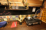 RV rental kitchen showing a portable stove, wooden utensils, blue plates, and a 'Happy 49th Birthday' chalkboard message.