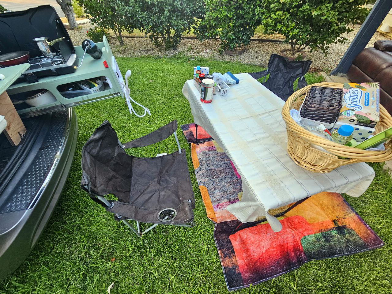 RV rental outdoor kitchen and dining setup on grass with chairs & picnic basket. — photo 19