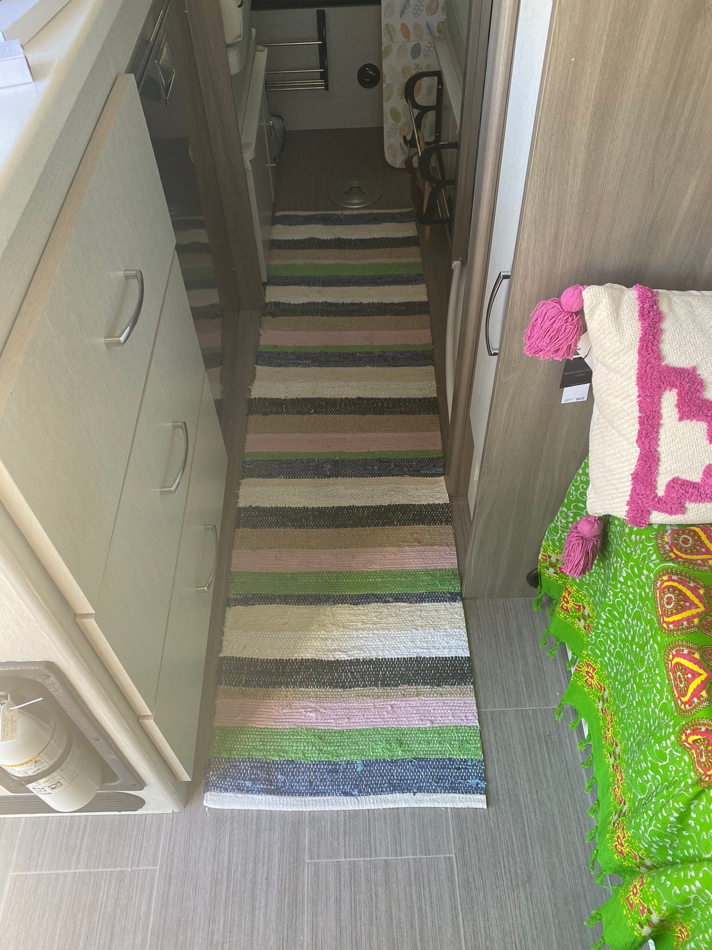 RV rental interior: A striped rug lines the hallway, flanked by light wood cabinets and a colorful bedding area leading to the bathroom. — photo 5