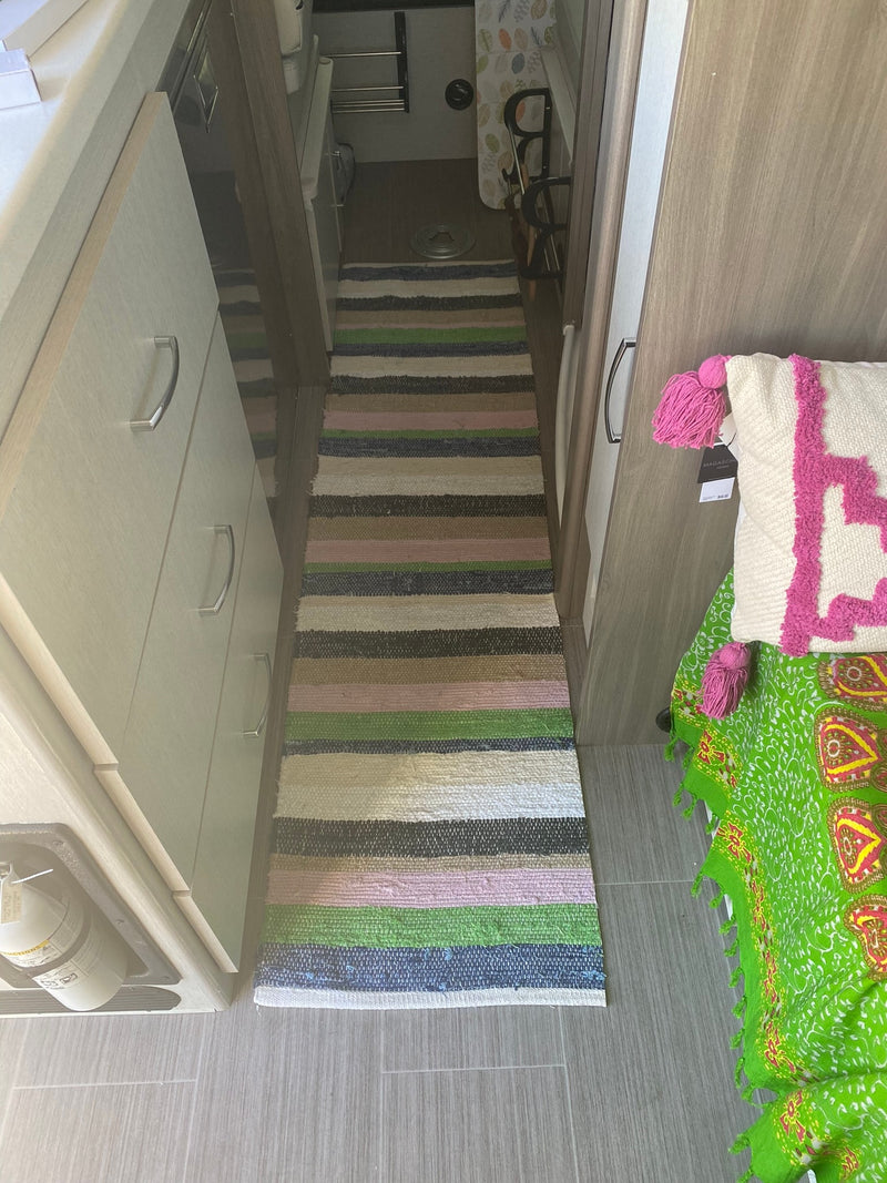 RV rental interior: A striped rug lines the hallway, flanked by light wood cabinets and a colorful bedding area leading to the bathroom. — photo 5