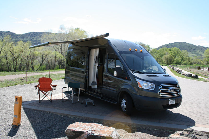 Gray Ford Transit RV rental camper van with extended awning & chairs at a scenic mountain campsite, ready for outdoor travel. — photo 1