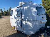 Compact white travel trailer, named Skyler, parked at a sunny campsite. Ideal for an rv rental adventure.