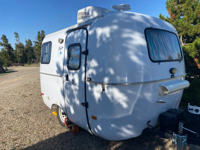 Compact white travel trailer, named Skyler, parked at a sunny campsite. Ideal for an rv rental adventure.