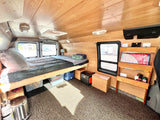 Experience van life in this RV rental: a wood-paneled camper with a bed, windows, and storage for travel.
