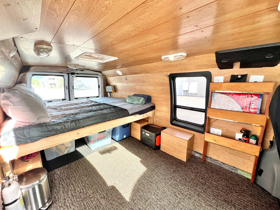 Experience van life in this RV rental: a wood-paneled camper with a bed, windows, and storage for travel.
