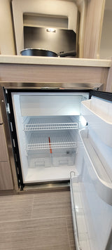 New, empty compact fridge/freezer in an rv rental kitchen, ready for your travel essentials. Shows shelves and drawers.