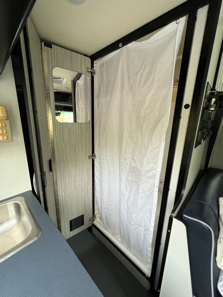 Compact RV rental interior featuring a shower with white curtain, adjacent to a small sink and kitchenette area.