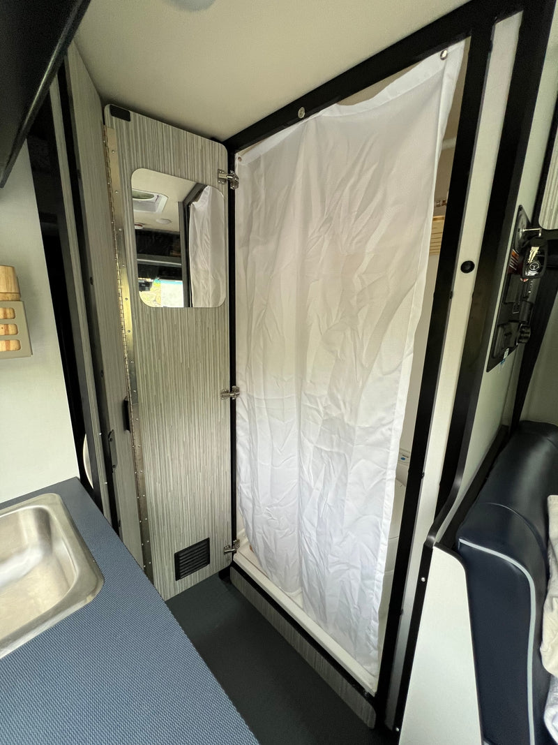 Compact RV rental interior featuring a shower with white curtain, adjacent to a small sink and kitchenette area. — photo 11