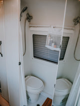 A compact, modern RV rental bathroom features a toilet, shower, and a mesh caddy with toiletries.