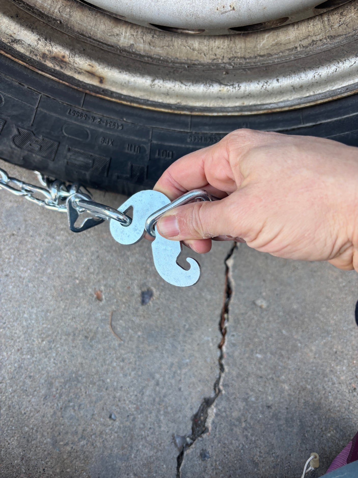 Hand attaching snow chains to an RV rental tire, essential for winter travel safety and traction on snowy roads.