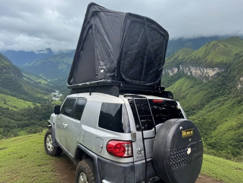  overlooks a stunning green mountain valley under a cloudy sky.|Silver FJ Cruiser with rooftop tent on a stunning beach — photo 3
