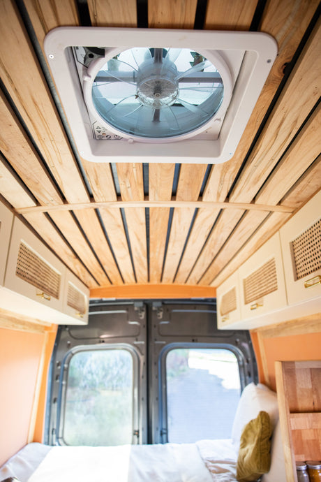 Looking up inside an RV rental: wood-slat ceiling, rooftop vent, overhead cabinets, and bed in a cozy camper van.