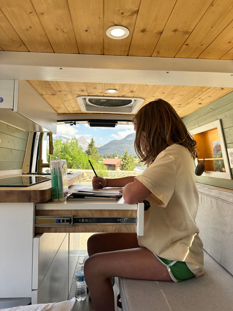Cozy RV rental workspace: girl drawing at a desk with mountain views. Ideal for van life travel & creativity.