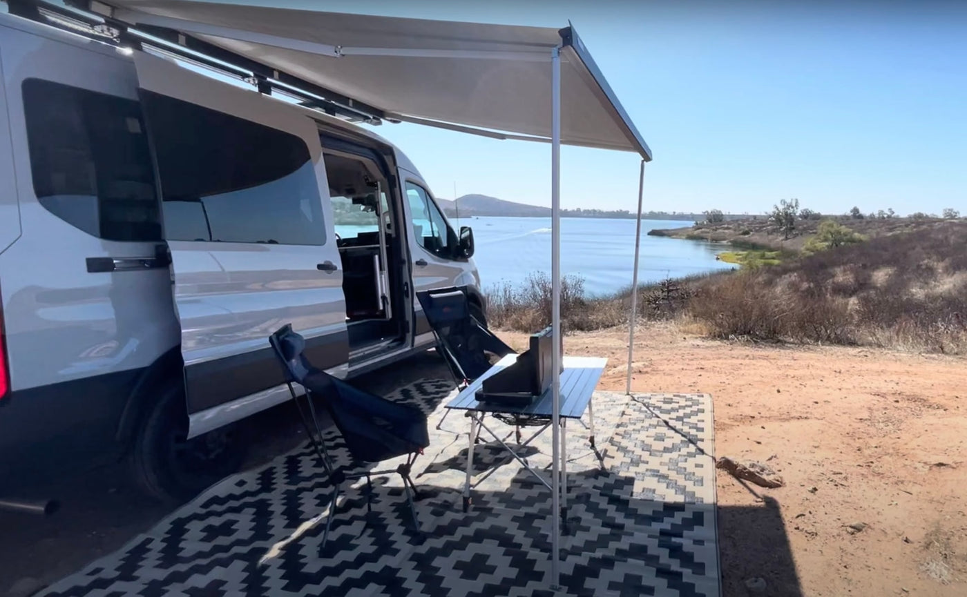Enjoy nature with an RV rental! White camper van by a lake with awning, table, and chairs set up for outdoor living. — photo 14