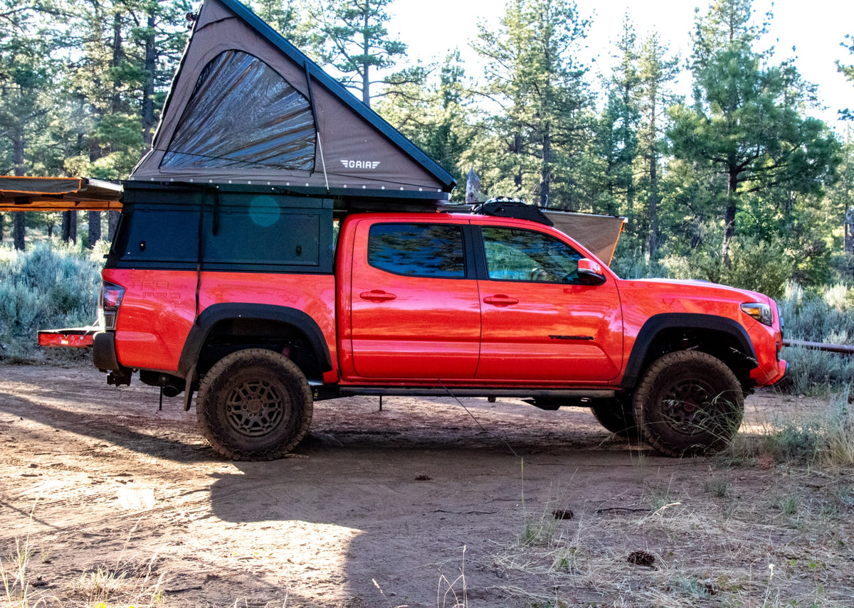 Red Toyota Tacoma with rooftop tent & awning setup for adventure. Perfect for your next overland rv rental trip!|Adventure-ready red Toyota Tacoma truck with an open rooftop tent and awning. An ideal RV rental for overlanding and truck camping.|Orange Tacoma overlander with pop-up tent & open bed storage in a sunny forest. Perfect RV rental alternative for adventure.|Vibrant orange Toyota Tacoma with an open rooftop tent