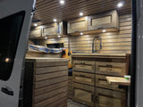 Cozy RV rental interior showcasing custom wooden cabinetry, a bed, and kitchenette.