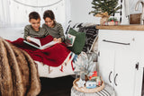 Cozy RV rental scene: Two kids reading a book under a red blanket, surrounded by holiday decor in their tiny home.
