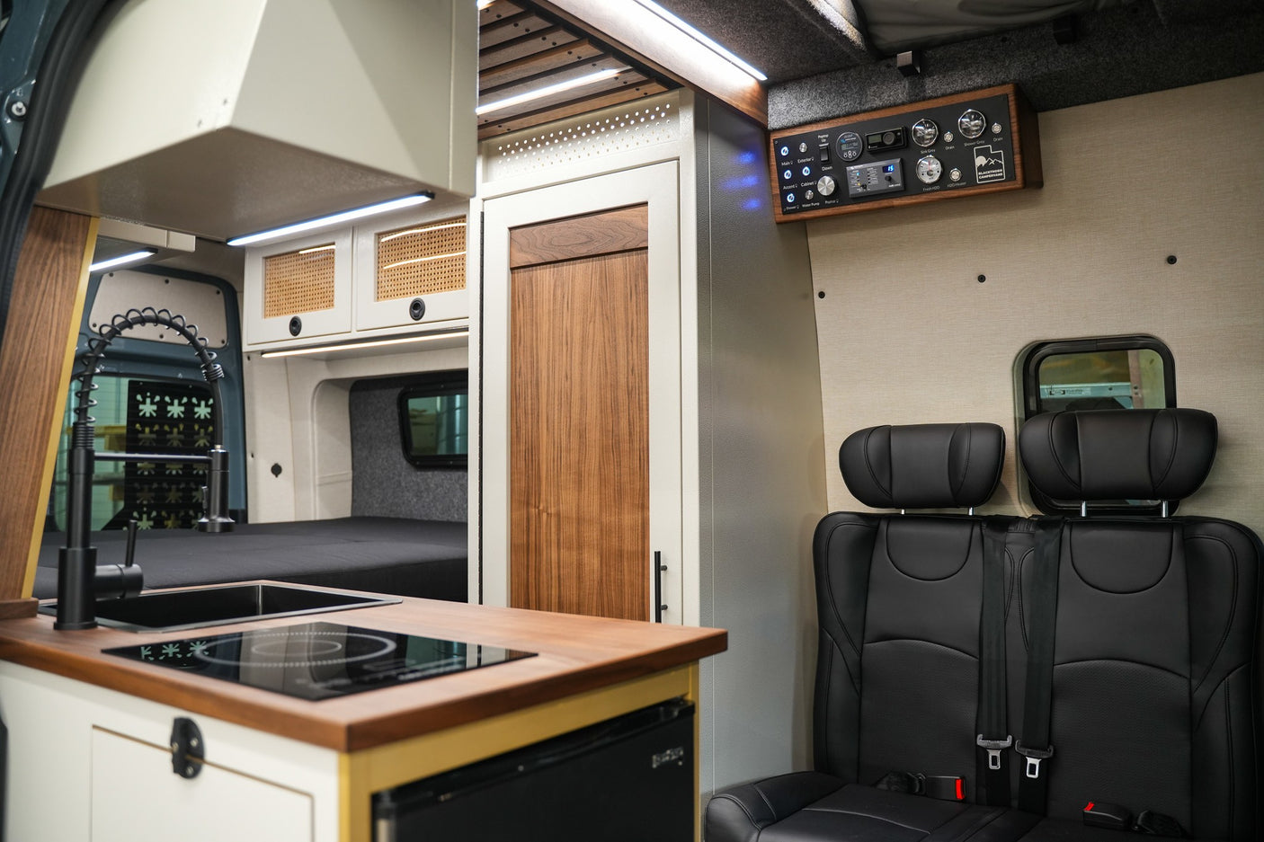 This RV rental interior features a modern kitchen, comfortable seating, a rear bed, and a control panel for mobile living.