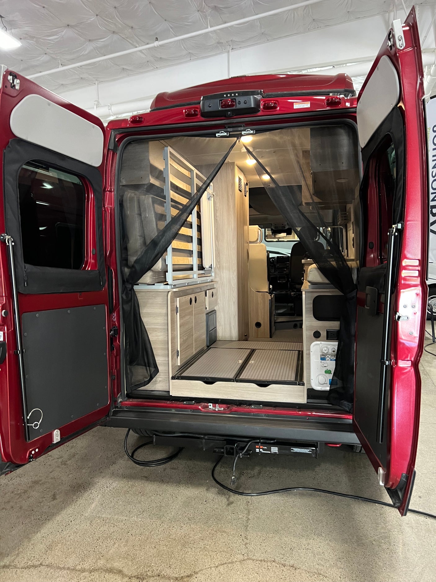 Experience adventure with this RV rental! Rear view of a red camper van interior, showcasing compact living space, cabinetry, and a mosquito net.