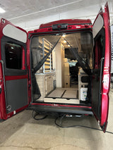Experience adventure with this RV rental! Rear view of a red camper van interior, showcasing compact living space, cabinetry, and a mosquito net.