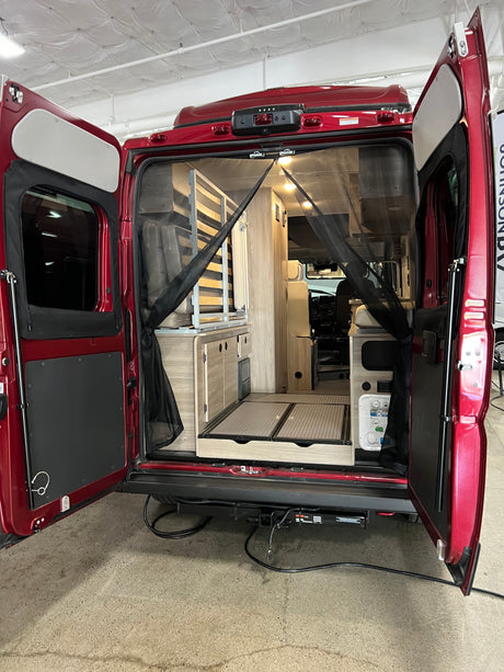 Experience adventure with this RV rental! Rear view of a red camper van interior, showcasing compact living space, cabinetry, and a mosquito net.