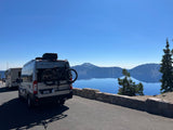RV rental: A Tellaro camper van with a bike rack overlooks a stunning blue lake and mountains under a clear sky.