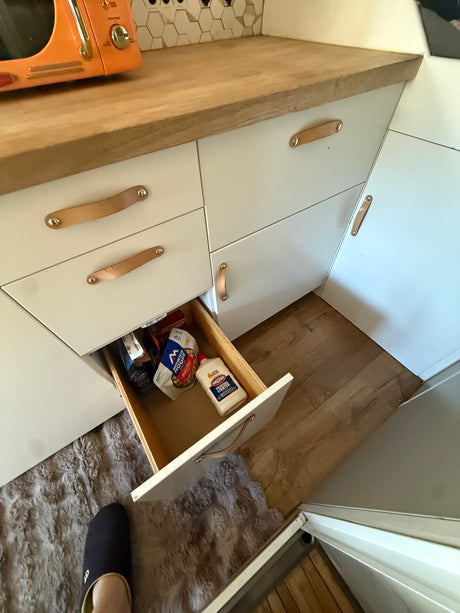 RV rental kitchen storage: Open drawer with camping food & lighter fluid. Features microwave and wooden counter.