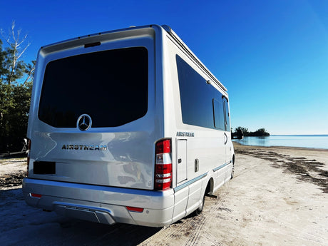 This Airstream RV rental sits on a sun-drenched beach by the ocean. Its rear features Mercedes badging and sleek design.