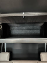 Open overhead storage in an RV rental, revealing a dark, lined interior above light-colored passenger seats.
