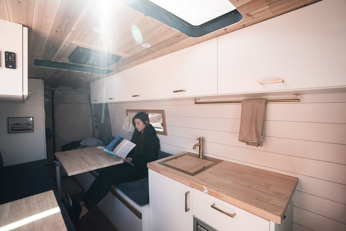 Cozy RV rental interior with a woman reading at a table, featuring a modern kitchen and wooden accents. — photo 3