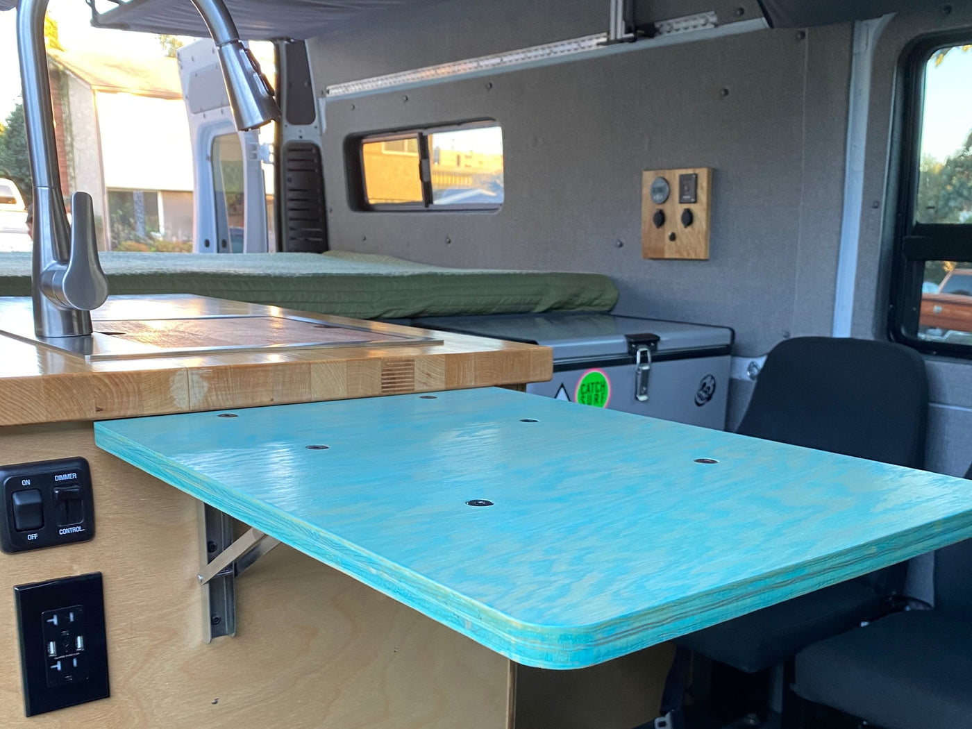 Inside this rv rental: a compact kitchen with modern faucet, wood counter, pull-out turquoise table, bed, & portable fridge. — photo 16