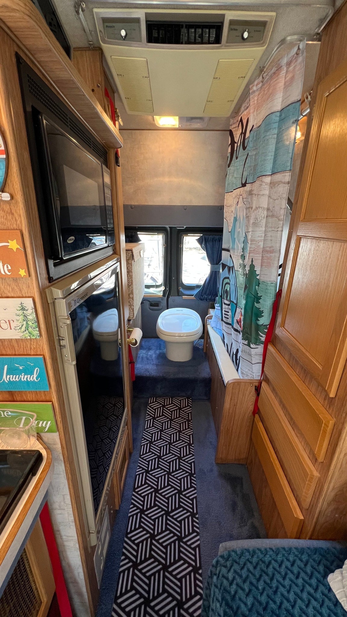  parked among bare trees and a hillside on a sunny day.|Step into this welcoming RV rental interior! Features a cozy living area with a blue couch — photo 6