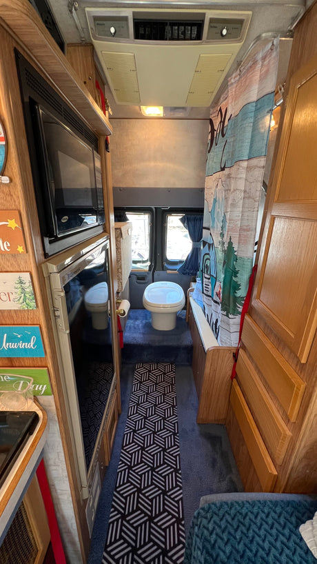 Interior view of an rv rental: compact kitchen w/ microwave & fridge, plus a rear bathroom with toilet & unique shower curtain. Cozy travel!