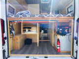 Rear view of an RV rental's well-designed camper van conversion, featuring a raised bed, organized storage, water tank, & fire extinguisher.