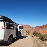 Scenic rv rental van adventure: white van with open door on a desert road, majestic red cliffs under clear sky.