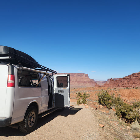 Scenic rv rental van adventure: white van with open door on a desert road, majestic red cliffs under clear sky.